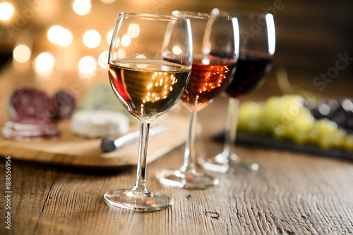three glass of red wine, rose wine and white wine with french cheese and delicatessen in restaurant wooden table with romantic dim light and cosy atmosphere