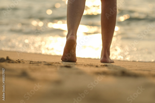 Fototapeta Naklejka Na Ścianę i Meble -  leg a girl walking on the beach with sunset light by walk barefoot