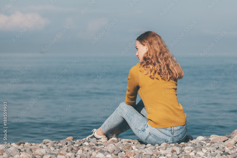 beautiful blonde girl is sitting on the beach and looking at the horizon