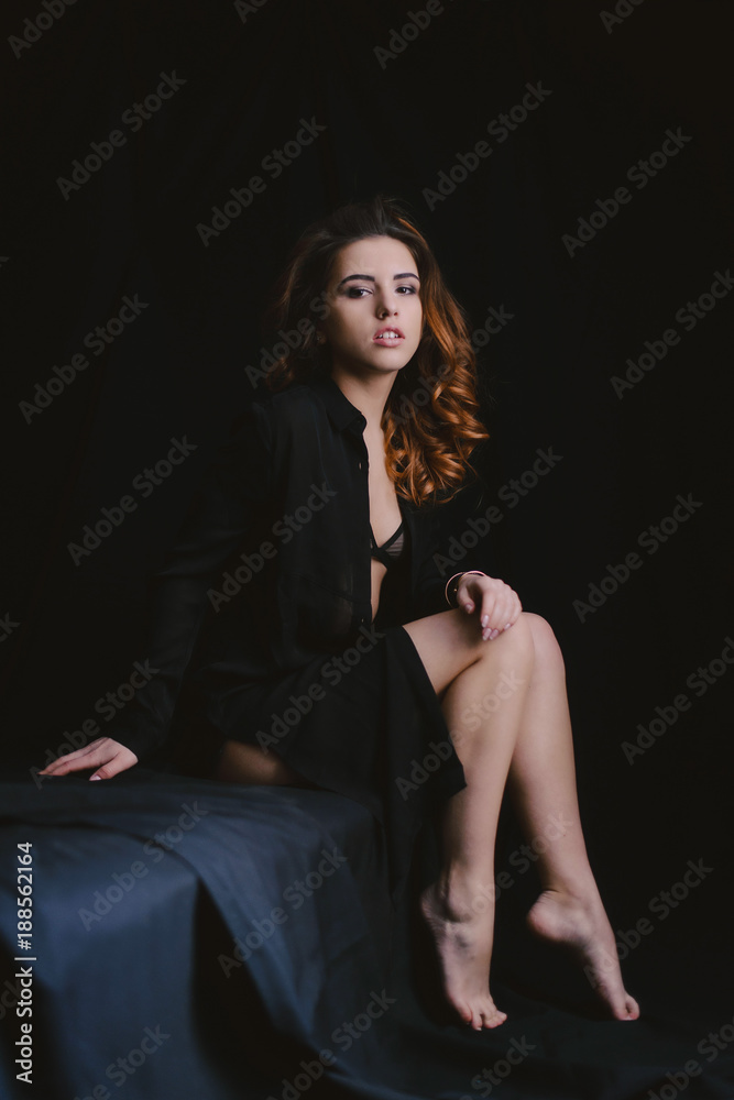 Beautiful girl with long curly hair, dressed in a black dress, posing on black background. Fashion style and poses Beautiful girl with long curly hair, dressed in a black dress, posing on black background. Fashion style and poses