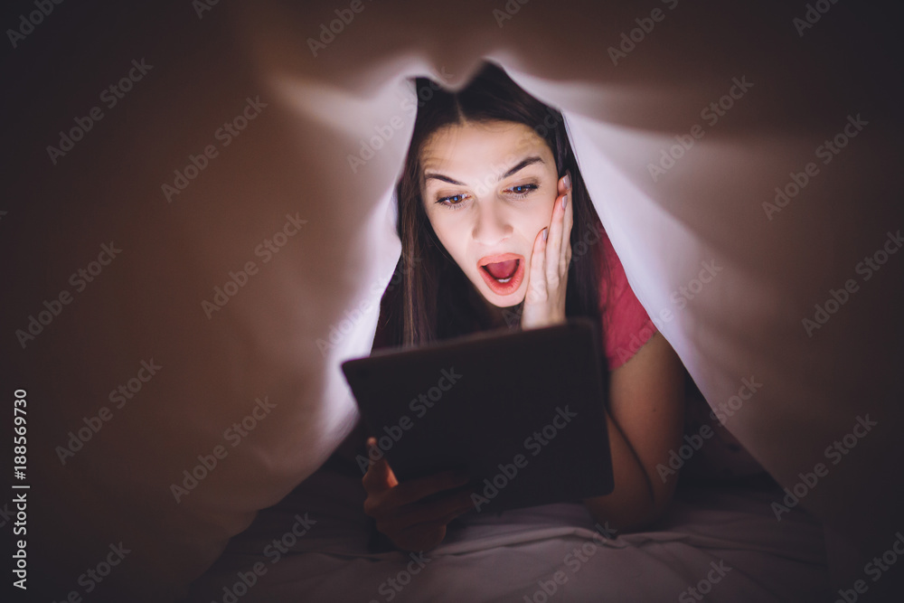 Pretty girl in sleepwear lying under blanket and surfing the internet. Pretty girl in sleepwear lying under blanket and surfing the internet.