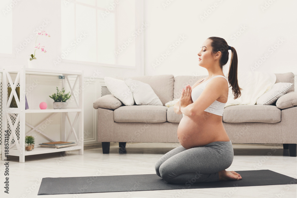 Happy pregnant woman training yoga in hero pose