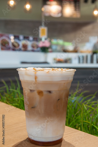 Gold caramel topping on white cream in coffee cup with green grass background.