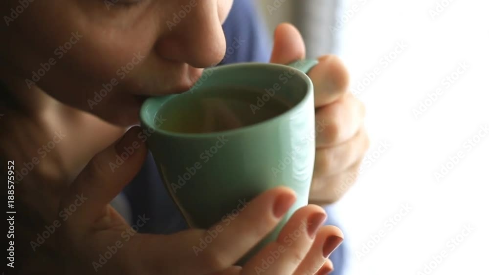 a young woman sits by the window and drinks hot tea from a glass a young woman sits by the window and drinks hot tea from a glass