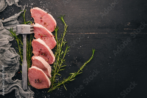 Raw meat. Beef steak with rosemary and spices on a black wooden background. Top view. Free space for text.