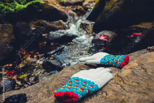 Natural background. Maple leaves on the rocks at the waterfall. Winter gloves placed on the stone. photo