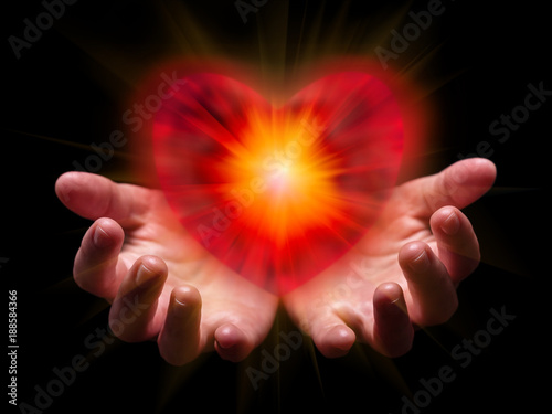 Hands cupped and holding or showing romantic red heart for Valentine or Valentines Day with bright, glowing, shining light. Concept for offering, giving in love, passion, romance. Black background