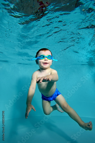 A young child swims underwater and plays with glasses for swimming. Portrait. Vertical orientation. The view from under the water