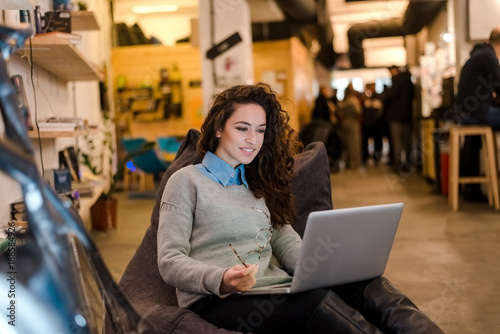 Beautiful young woman working on laptop and smiling while sitting indoors.