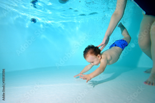 The kid dives to the bottom of the pool  and the coach helps him. Portrait. Horizontal orientation