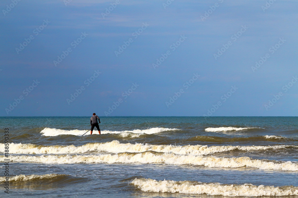 Standup paddle board surfer (SUP) surfing has caught the wave and has fun surfing on wave of Black Sea against the background of dark blue stormy sky