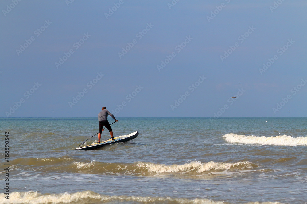 Fototapeta premium Standup paddle board surfer (SUP) surfing has caught the wave and has fun surfing on wave of Black Sea against the background of dark blue stormy sky