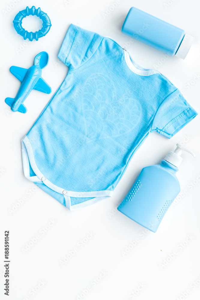Blue baby clothes for little boy. Bodysuit, toys, cosmetics on white background top view copy space Blue baby clothes for little boy. Bodysuit, toys, cosmetics on white background top view copy space