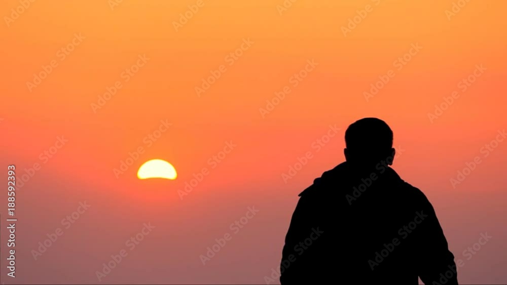 Silhouette of a young guy looking at an orange Sunset