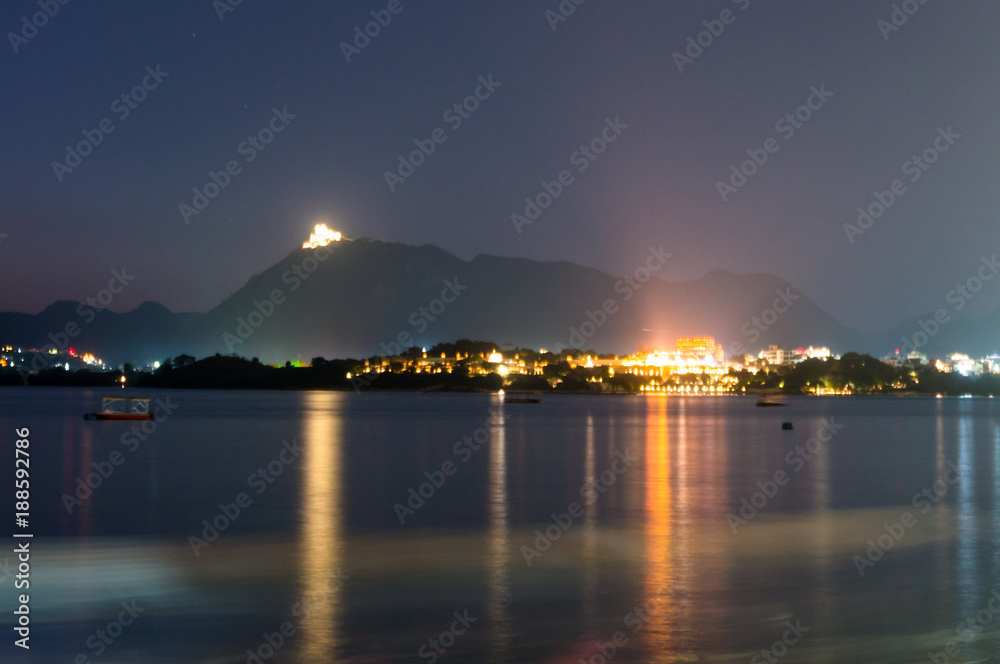 Foggy night shot of udaipur city at the base of the aravali hills with the city lights and light from a temple at the top of the hill clearly visible. Udaipur is a beautiful city in india, must visit Foggy night shot of udaipur city at the base of the aravali hills with the city lights and light from a temple at the top of the hill clearly visible. Udaipur is a beautiful city in india, must visit