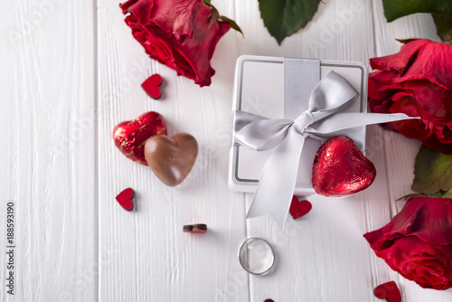 Fresh red roses and gift box on wooden table