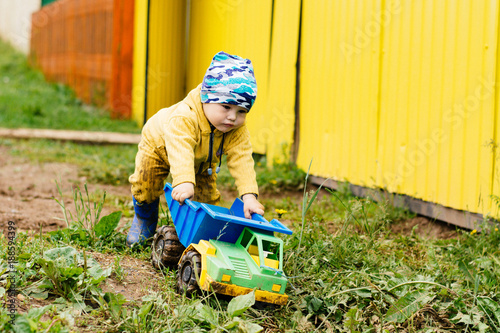 the boy in yellow suit playing with a toy car in the dirt photo