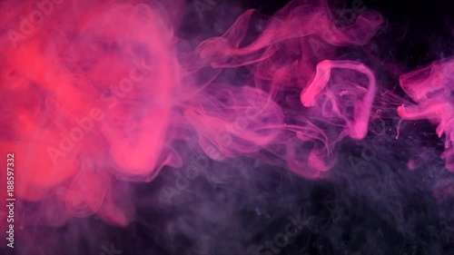 Abstract red neon flowing ink in water over black background. Dropping colorful ink into the water. Slow motion 4K UHD video footage. 3840X2160