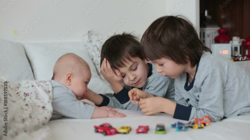 Three children, baby and his older brothers in bed in the morning, playing together, laughing and having a good time, sharing special moment, bonding Three children, baby and his older brothers in bed in the morning, playing together, laughing and having a good time, sharing special moment, bonding
