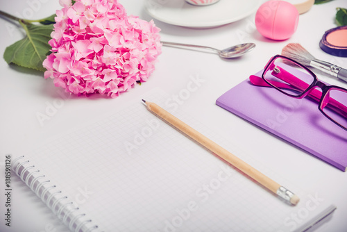 Top view Female working place with notebook for planning, cosmetic, sketchbook, glasses, and wisteria flowers on the white background. Fashion, Beauty blog concept. photo