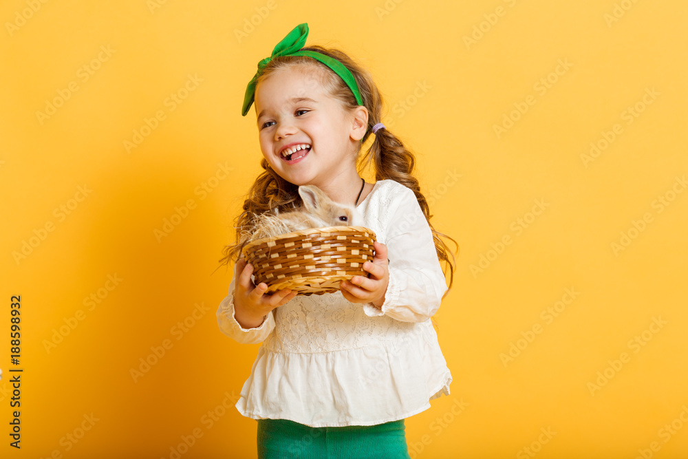 Pretty happy child girl is holding her friend little colorful rabbit, Easter holiday concept isolated on yellow