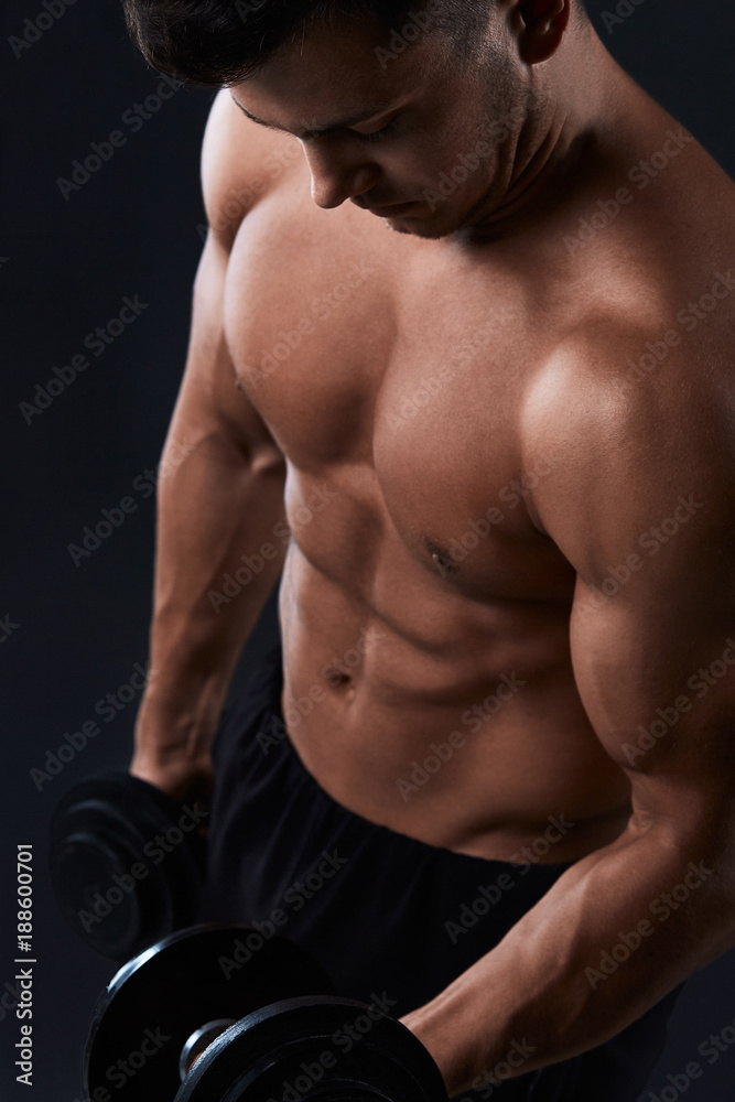 Muscular bodybuilder doing exercises with dumbbell over black background.Strong athletic man shows body,abdominal muscles,biceps and triceps.Work out,gaining weight,pumping up muscles with dumbbells. Muscular bodybuilder doing exercises with dumbbell over black background.Strong athletic man shows body,abdominal muscles,biceps and triceps.Work out,gaining weight,pumping up muscles with dumbbells.