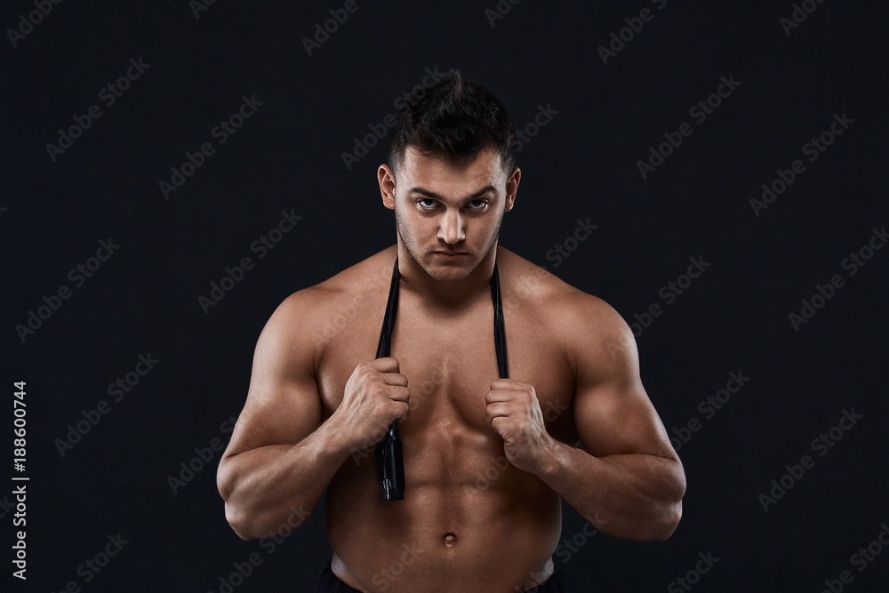 Muscular bodybuilder with jump rope on black background.Strong athletic man shows body,abdominal muscles,chest muscles,biceps and triceps.Work out,gaining weight. Bodybuilding concept.