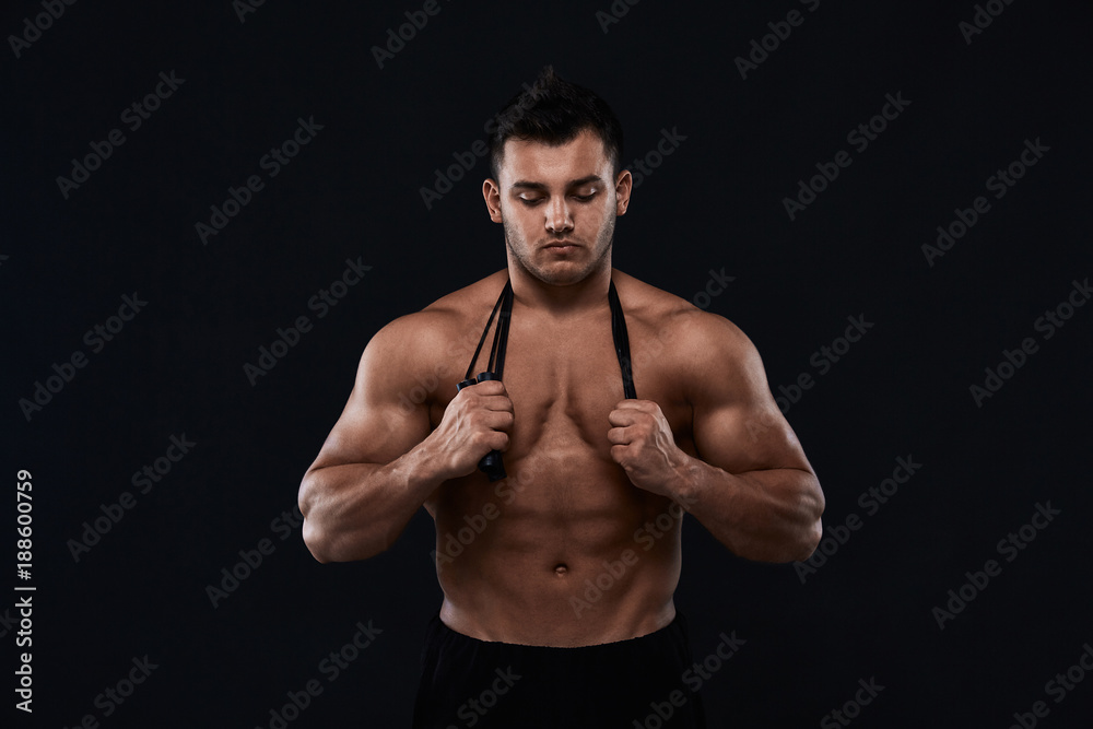Muscular bodybuilder with jump rope on black background.Strong athletic man shows body,abdominal muscles,chest muscles,biceps and triceps.Work out,gaining weight. Bodybuilding concept.