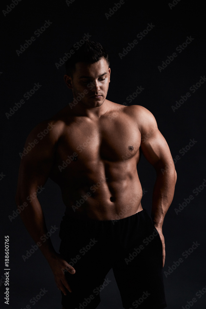 Muscular bodybuilder on black background.Strong athletic man shows body,abdominal muscles,chest muscles,biceps and triceps.Work out,gaining weight. Bodybuilding concept.