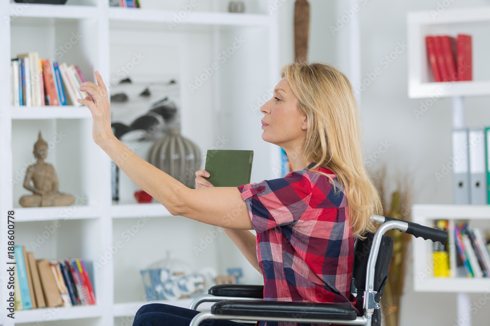 disabled woman trying to get book wheelchair in living room disabled woman trying to get book wheelchair in living room