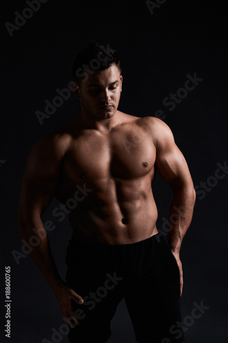Muscular bodybuilder on black background.Strong athletic man shows body,abdominal muscles,chest muscles,biceps and triceps.Work out,gaining weight. Bodybuilding concept. © YURII MASLAK