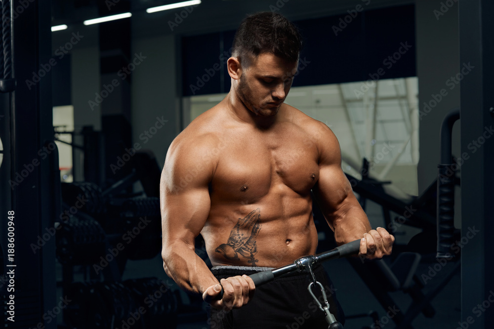 Muscular bodybuilder doing exercises on cable crossover machine in gym.Strong athletic man shows body,abdominal muscles,biceps and triceps.Work out,gaining weight,pumping up muscles. Muscular bodybuilder doing exercises on cable crossover machine in gym.Strong athletic man shows body,abdominal muscles,biceps and triceps.Work out,gaining weight,pumping up muscles.