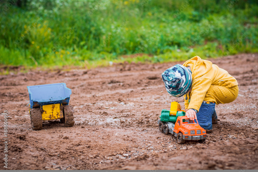 Fototapeta premium the boy in yellow suit playing with a toy car in the dirt