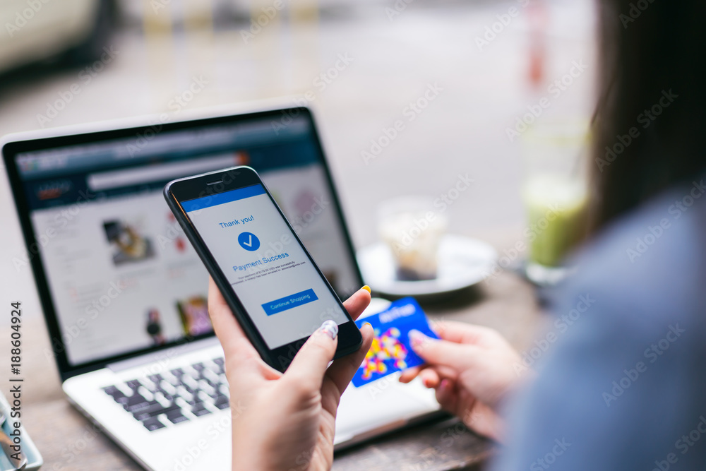 © Mymemo - Young asian woman making payment success on mobile smartphone screen and using credit card while shopping on online retail shop with laptop computer on table at coffee cafe, lifestyles technology