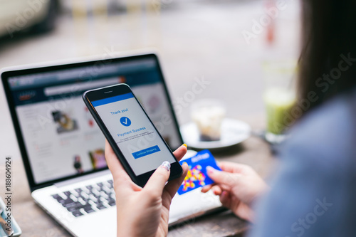 Young asian woman making payment success on mobile smartphone screen and using credit card while shopping on online retail shop with laptop computer on table at coffee cafe, lifestyles technology