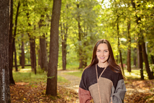 Portrait of a young woman brunette in a wool poncho Standing on a footpath in the green Park in the background in the rays of the bright sun