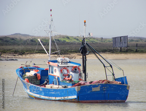 small blue wooden traditional fishing boat anchored in a natural harbor with calm water photo