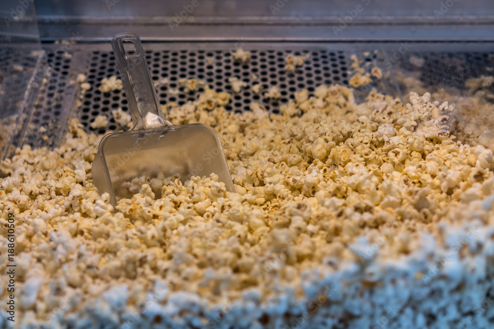A closed up look through glass cabinet of salted butter popcorn and serving scoop in incubator machine