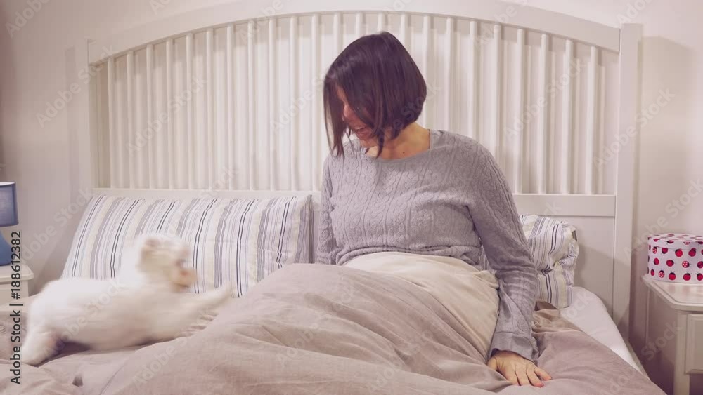 Happy woman in the morning playing with puppy dog jumping in bed retro style closeup Happy woman in the morning playing with puppy dog jumping in bed retro style closeup