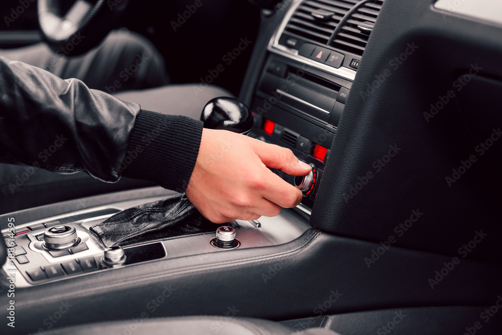 Driver regulates climate control in his stylish modern car. Close up man's hand driving a car