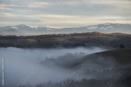 Mysterious fog covered hills in the foreground with the snow covered carpathian mountains in the background