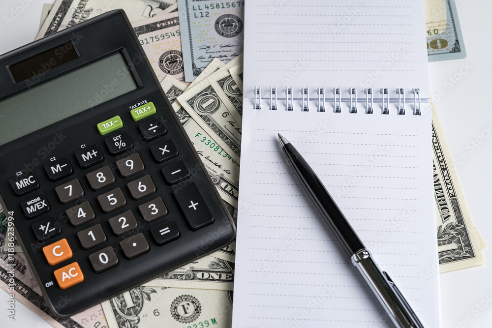 White paper note pad and pen, calculator on dollar banknotes using as business accounting or tax calculation concept White paper note pad and pen, calculator on dollar banknotes using as business accounting or tax calculation concept