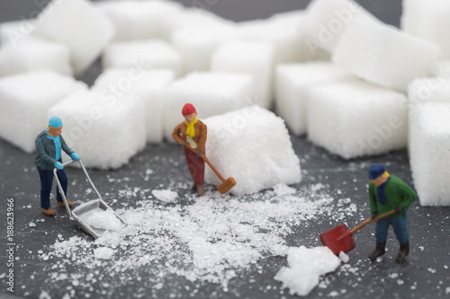 Miniature people sweep up sugar. Health care and snow concept.