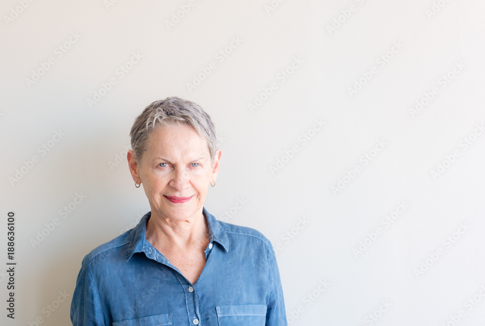 Beautiful older woman with short grey hair and striking blue eyes against neutral background Beautiful older woman with short grey hair and striking blue eyes against neutral background