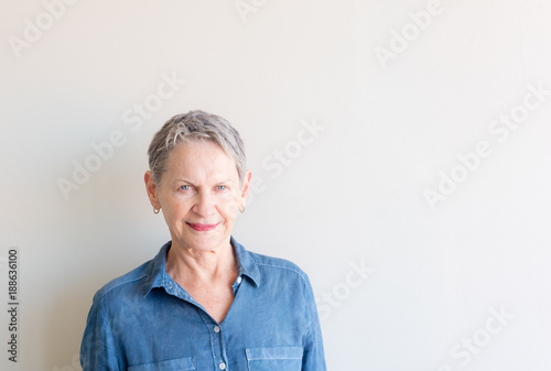 Beautiful older woman with short grey hair and striking blue eyes against neutral background