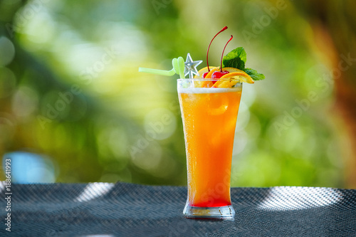Orange cocktail with ice in glass on the background of nature. Cocktail on the background of the bar. Orange alcoholic cocktail in a traditional glass. Place to write a recipe