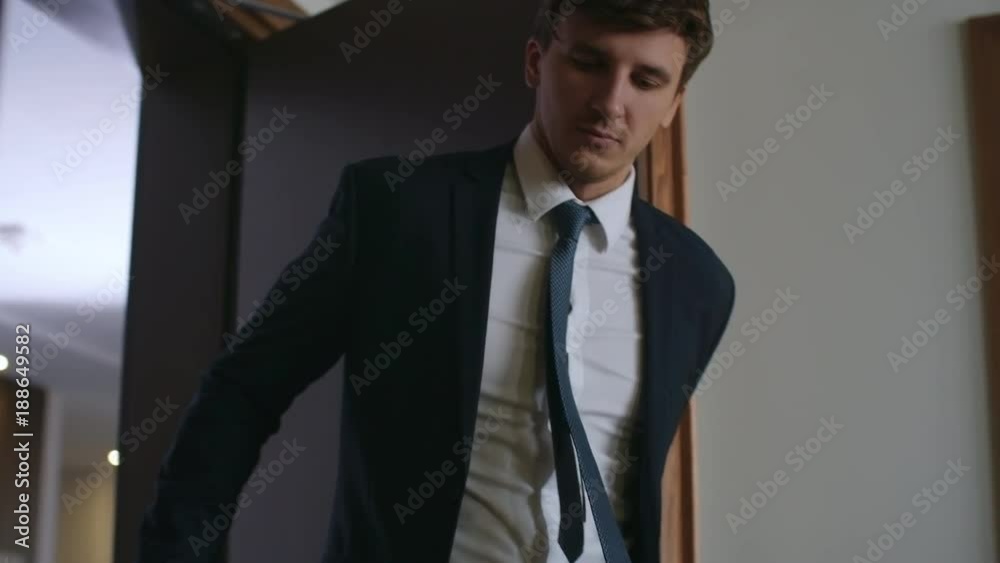 Young businessman in formal suit entering hotel room with luggage and closing the door