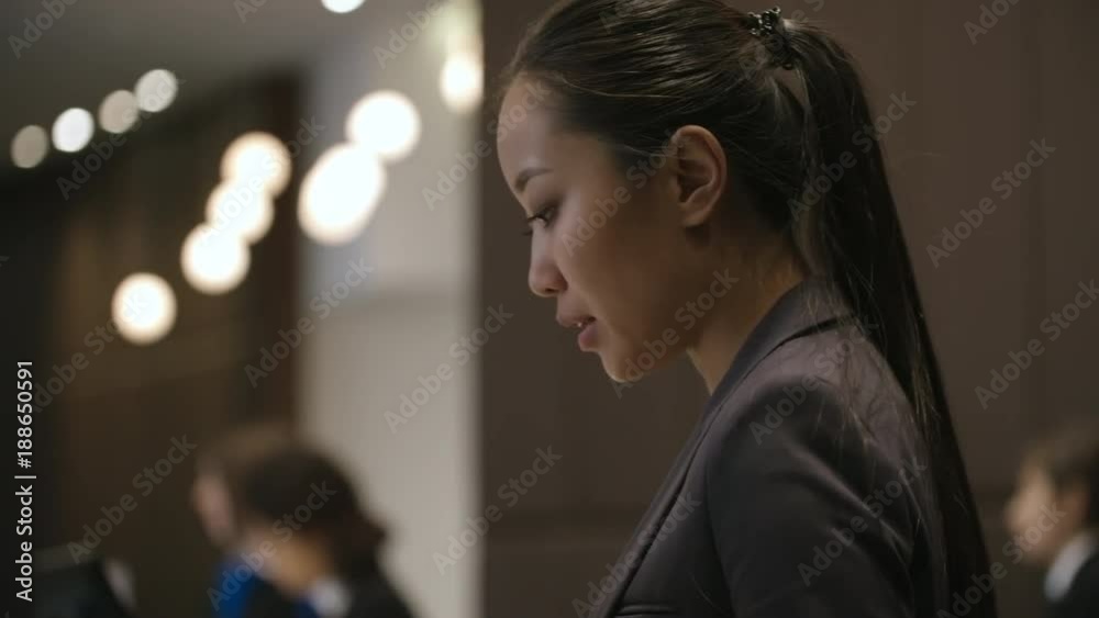 Young Asian receptionist working at front desk in hotel and talking to guests during check-in procedure