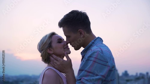 Loving couple passionately kissing, meeting dawn on roof of high-rise building