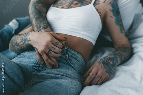 Fényképezés cropped view of tattooed couple holding hands and relaxing on bed